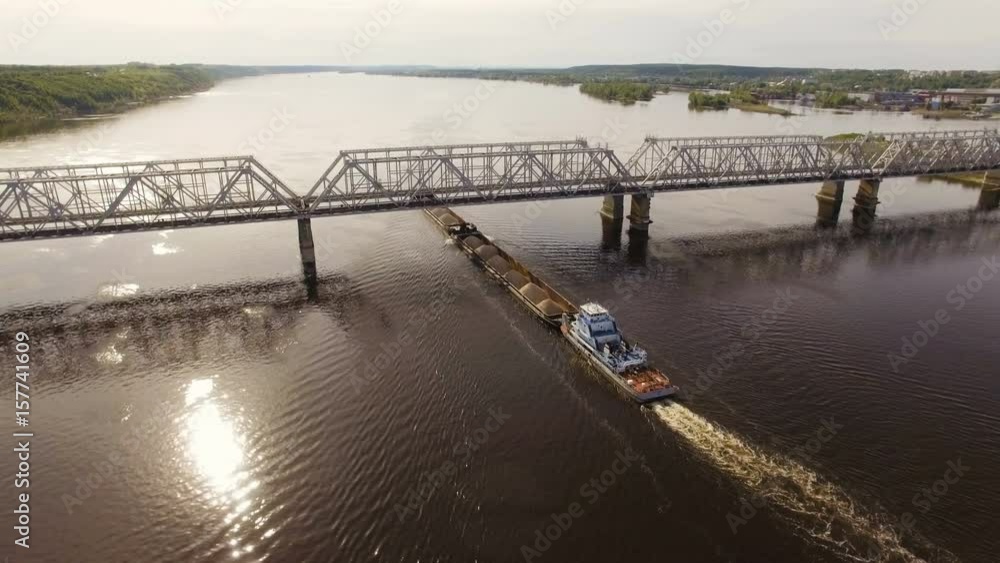 barge with sand and gravel sails under the railroad bridge across the river. Aerial view barge with sand and gravel sails under the railroad bridge across the river. Aerial view