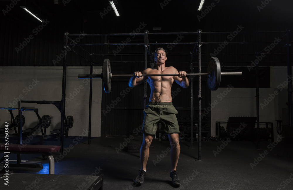Muscular White Caucasian man doing barbells snatch exercise in a dark grungy gym wearing shorts and showing muscular body and six pack abs Muscular White Caucasian man doing barbells snatch exercise in a dark grungy gym wearing shorts and showing muscular body and six pack abs
