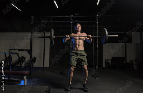Muscular White Caucasian man doing barbells snatch exercise in a dark grungy gym wearing shorts and showing muscular body and six pack abs 