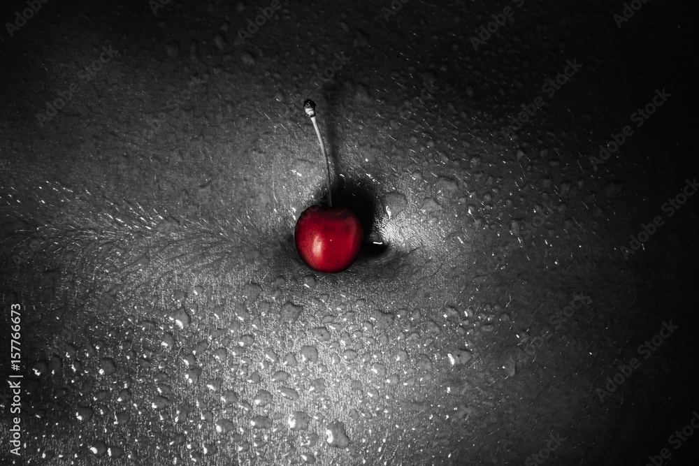 Red cherry on bare navel with drops of water or sweat black and white  photo. Naked