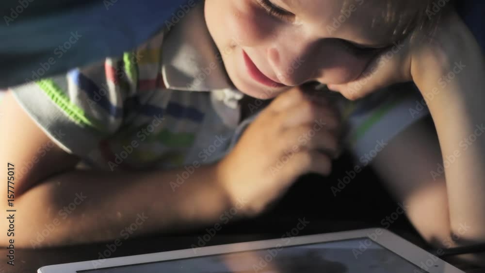 Boy lying under blanket and watching cartoon on touch pad Boy lying under blanket and watching cartoon on touch pad