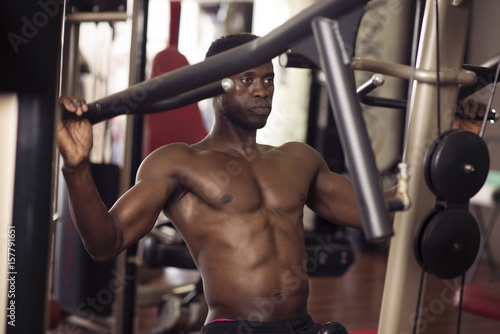 black man with naked torso doing exercises with a gym machine