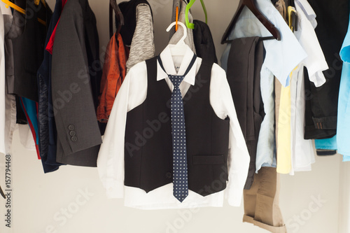 men's or boy's shirts with tie and waistcoat hanging on hangers in the white wardrobe