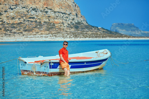 man standing in the sea near the boat. man wearing in red polo shirt and sunglass