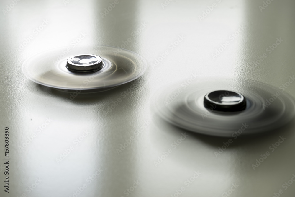 Long exposure with motion blur of two fidget spinners during fast rotation on an abstract background. Long exposure with motion blur of two fidget spinners during fast rotation on an abstract background.