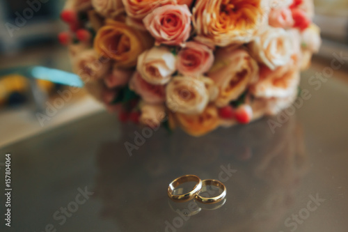 Wedding gold rings on a transparent table and a wedding bouquet