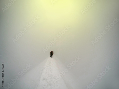 Mountaineer arrive to the summit of a snowy peak. Concepts: determination, courage, effort, self-realization. Clear sky, sunny day, winter season. Large copy-space on the left. European Alps, Europe