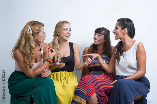 gruppo di amiche vestite con colori sgargianti, chicchierano amabilmente sedute - sfondo chiaro photo