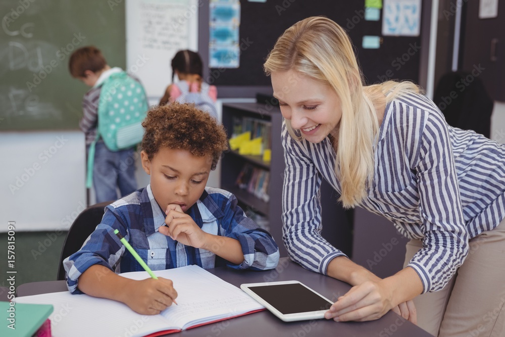 Teacher helping schoolboy with his homework in classroom Teacher helping schoolboy with his homework in classroom