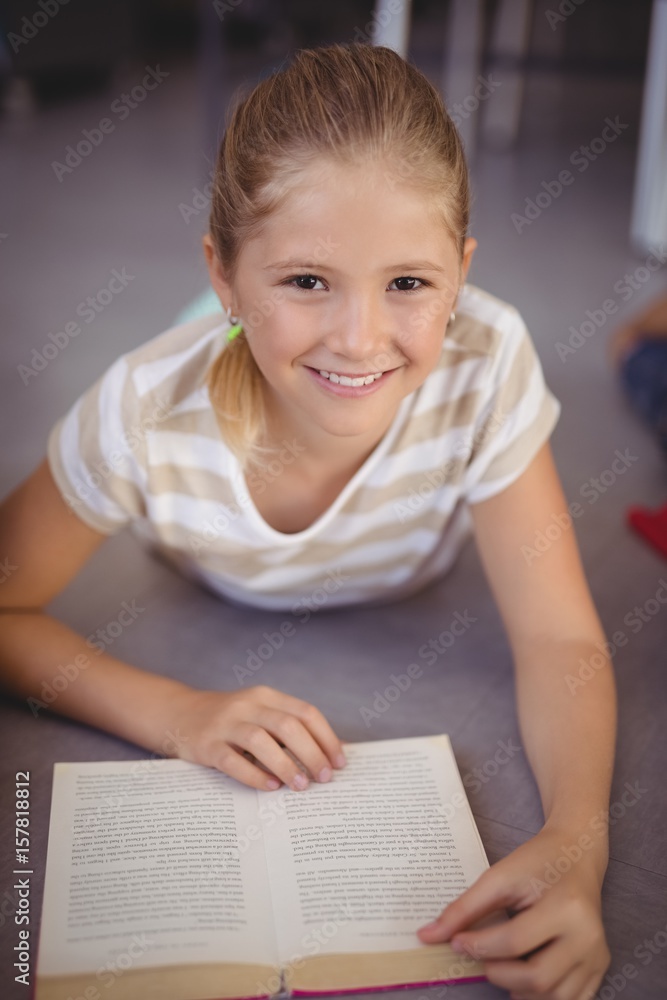 Portrait of happy schoolgirl reading book in library Portrait of happy schoolgirl reading book in library