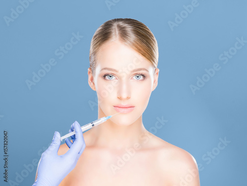 Young and beautiful woman having skin injections over cyan background. Plastic surgery concept.