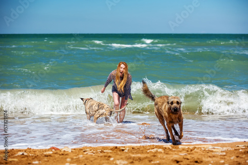 Beautiful young woman with long hair on the seashore or the ocean is an ative run and plays with two dogs, she laughs and rejoices. photo