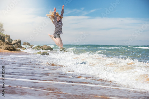 Beautiful sports young woman on a tropical ocean coast jumping high above the waves.