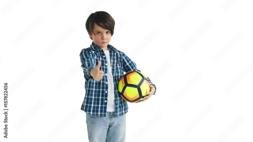 Little soccer player on a white background seriously looking at the camera and gives a thumbs up Little soccer player on a white background seriously looking at the camera and gives a thumbs up