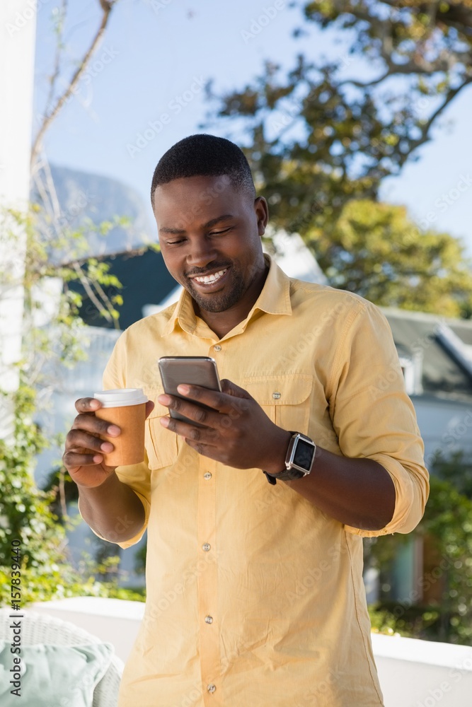 Young man using mobile phone while holding coffee cup at cafe Young man using mobile phone while holding coffee cup at cafe