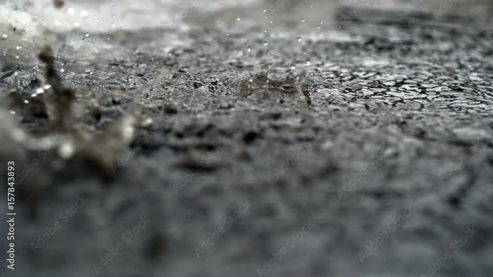 Slow motion rain drops in a dirty puddle