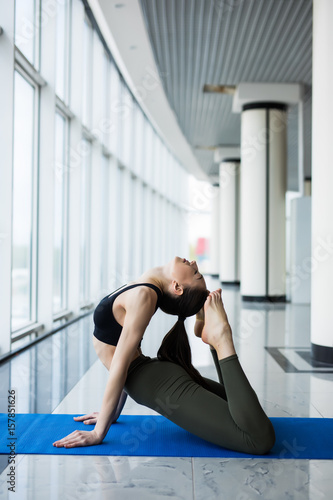 One-Legged King Pigeon Pose. Woman yoga practice pose training concept in gym hall with big windows photo