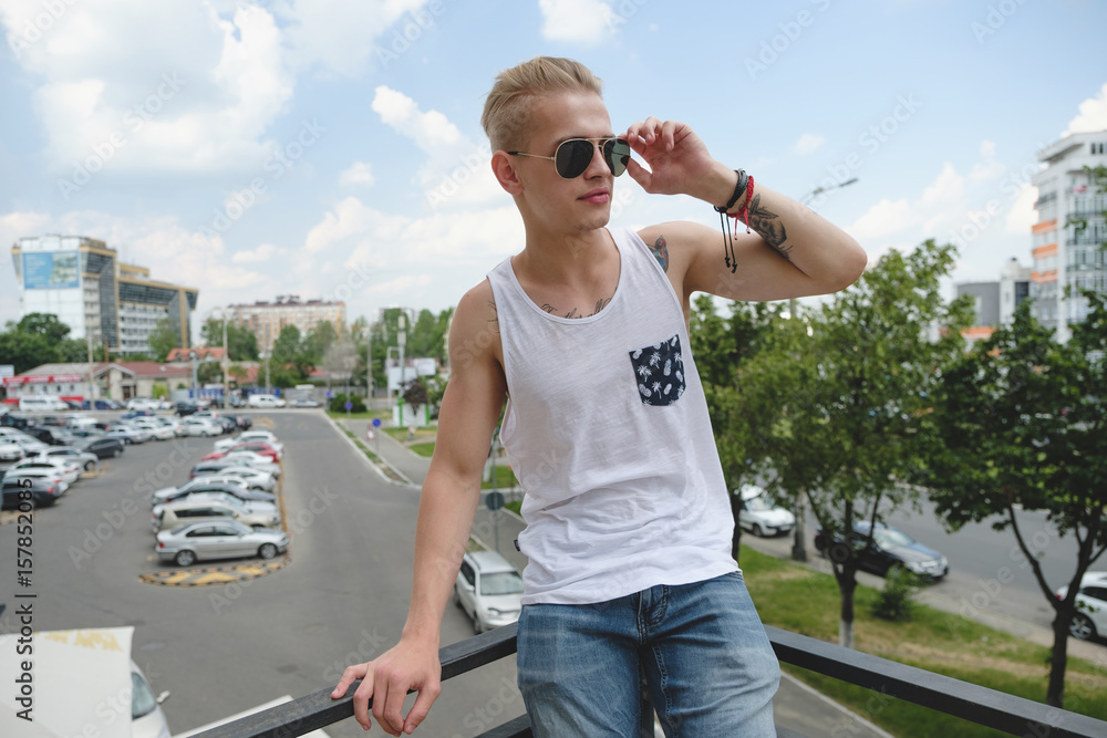 Hipster handsome man guy in stylish summer clothes in the street in sunglasses