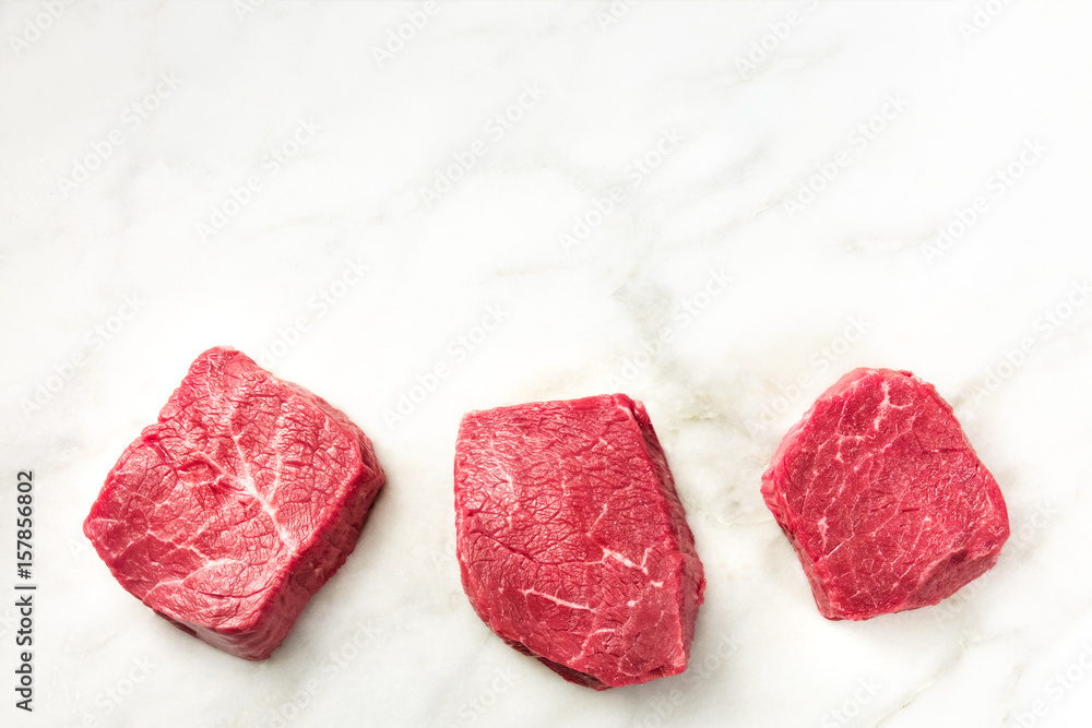 Three slices of raw meat on white marble with copyspace Three slices of raw meat on white marble with copyspace