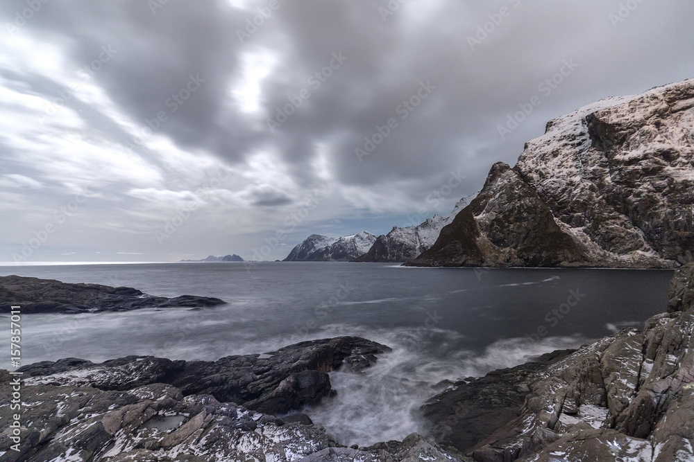 Cloudy sky above the mountains partially snowy and the cold sea. Lofoten Islands. Northern Norway. Europe