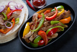 Cast-iron frying pan with mexican traditional fajitas, close-up, selective focus