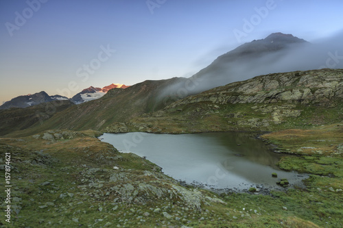 Mist at sunrise on the alpine lake in the background the snowy peaks Minor Valley Alta Valtellina Livigno Lombardy Italy Europe