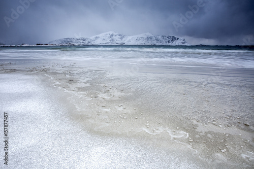 Waves of the icy sea on the beach in the background the snowy peaks Ramberg Lofoten Islands Norway Europe