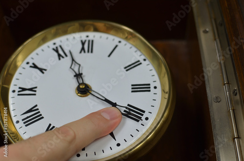 A finger on a hand of a vintage clock trying to stop it or trying to turn back time