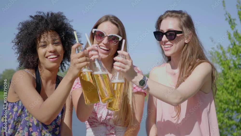 Three young black and white women standing and clinking beer with straws together. Three young black and white women standing and clinking beer with straws together.