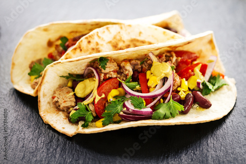 Beautiful tasty appetizing traditional mexican food tacos with meat and vegetables on black slate. Closeup.
