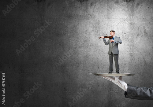 Businessman on metal tray playing violin against concrete background