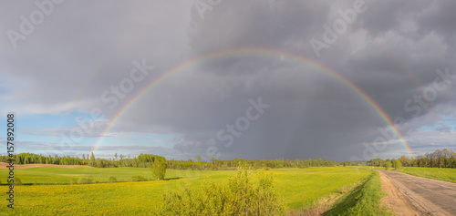 Colorful rainbow after the storm passing over a field near the road