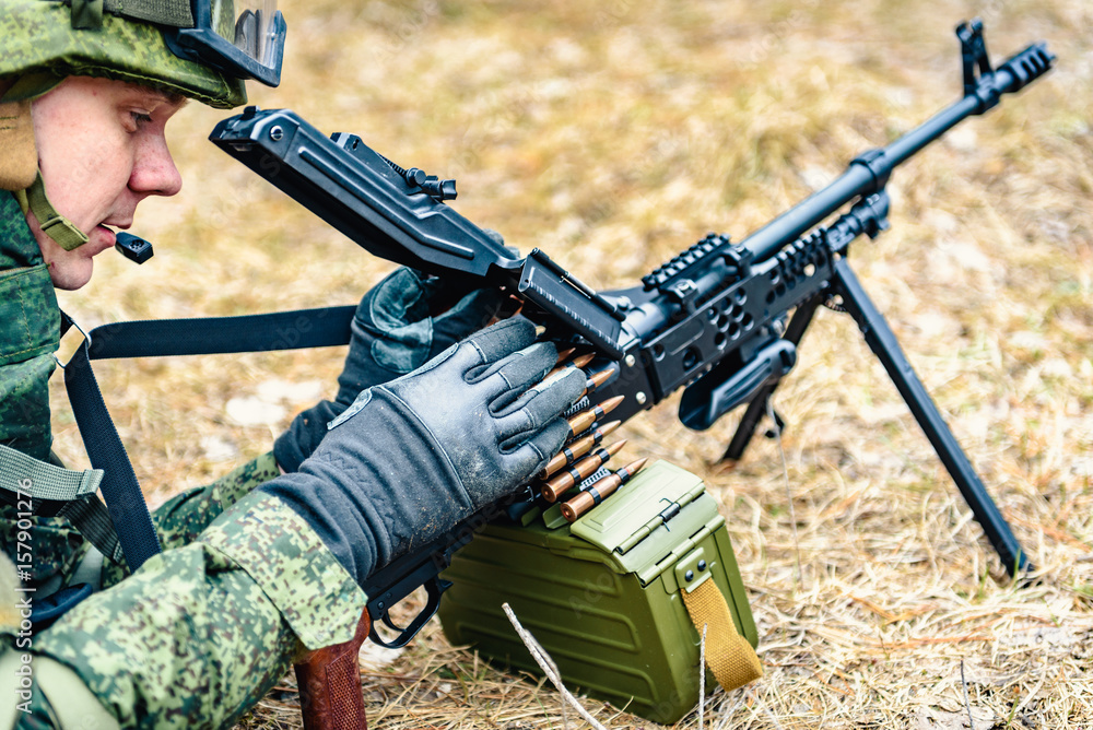 Automatic weapons in the hands of a soldier of the Russian army during a combat operation, against a background of coniferous forest and field Automatic weapons in the hands of a soldier of the Russian army during a combat operation, against a background of coniferous forest and field