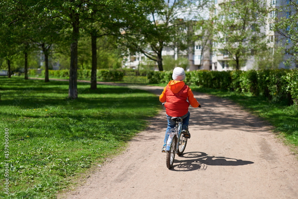 Fototapeta premium Small boy ride bicycle in street park. He is pointing moving dow