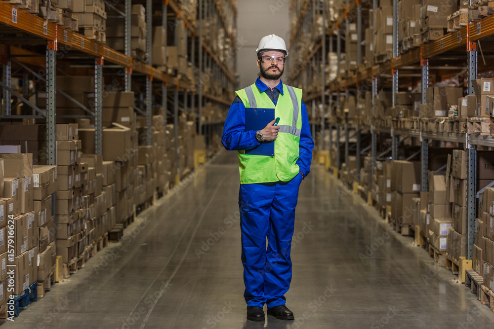 Warehouse worker standing between rows with merchandise and looking at camera Warehouse worker standing between rows with merchandise and looking at camera