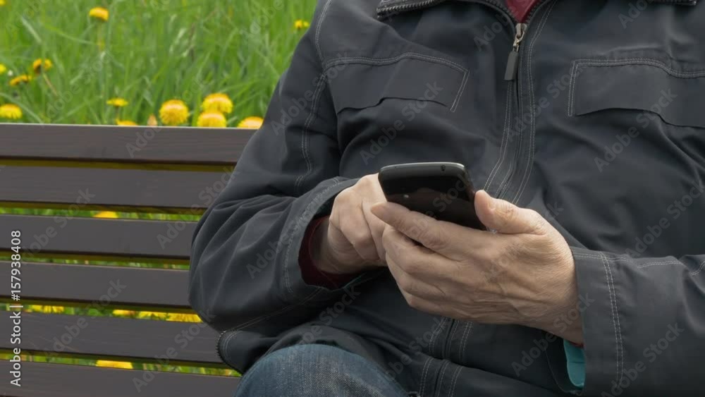 Elderly Man Sitting On Park Bench And Messaging On Mobile Phone Elderly Man Sitting On Park Bench And Messaging On Mobile Phone