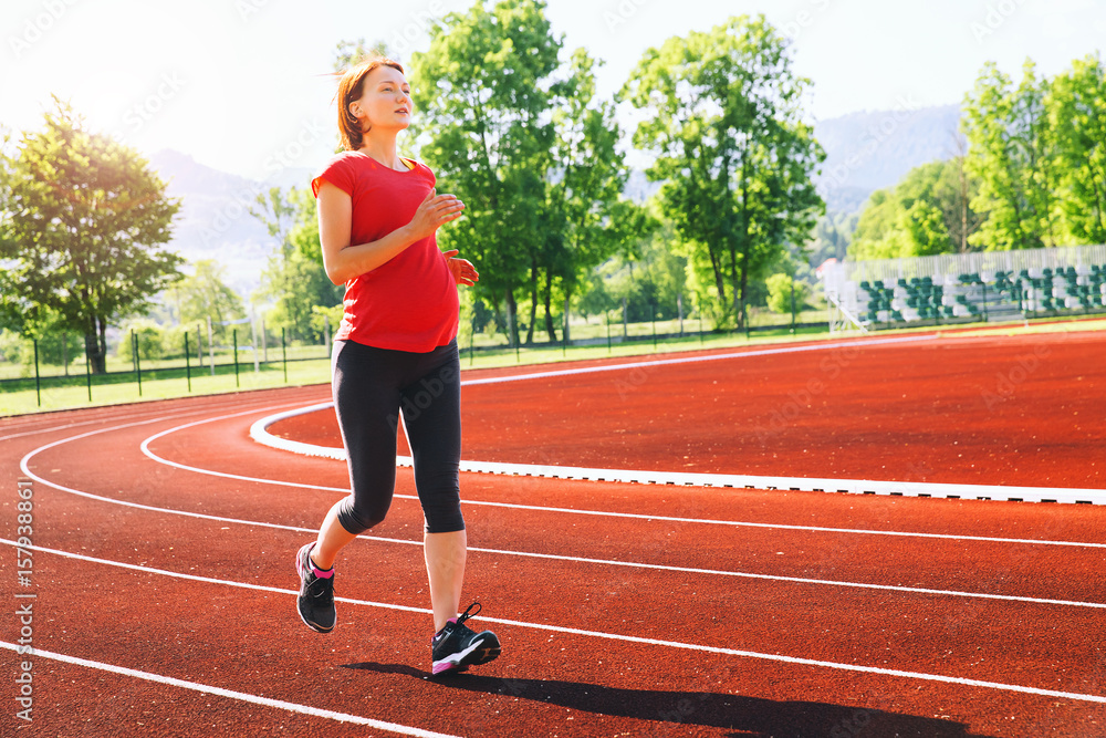 Fototapeta premium Pregnant woman jogging on running track in stadium.