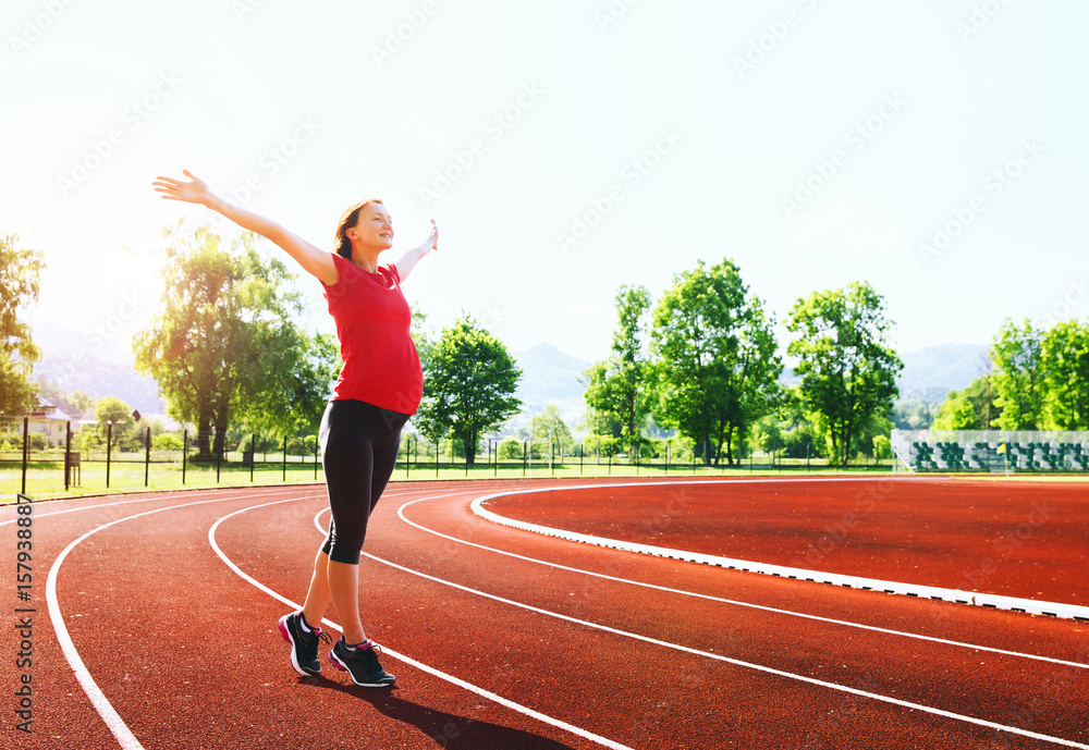 Happy pregnant woman with raised hands on sport stadium.