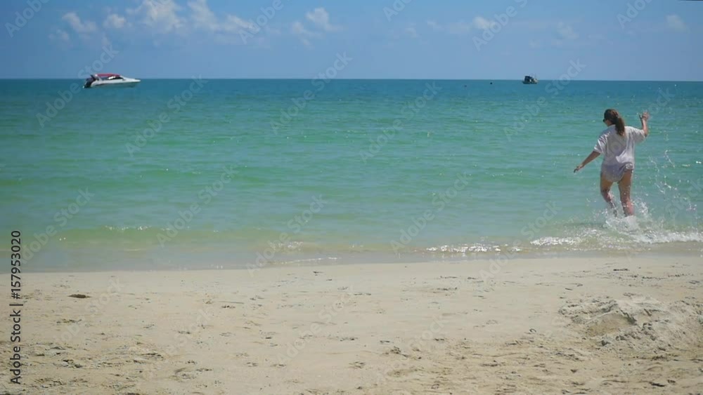 a young girl runs along the beach, creating a spray of water. Tropical island, on a hot day a young girl runs along the beach, creating a spray of water. Tropical island, on a hot day
