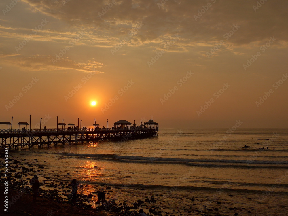 Orange glow of the setting sun low on the horizon over a crowded pier. 