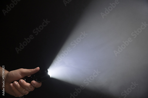 Male hand holding a led flashlight with a very wide white beam on a black background, leaving the left side of the frame