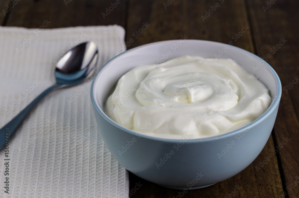 Natural yoghurt in bowl with spoon on rustic wooden table background Natural yoghurt in bowl with spoon on rustic wooden table background