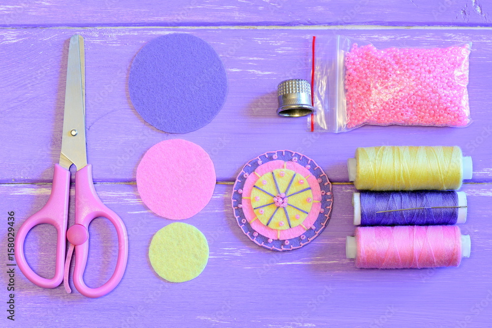 Fototapeta premium Making felt flower for pins, brooches, decorations or embellishments. Flower made of felt circles and beads, handcraft supplies on a wooden table. Sewing tutorial. Teaching sewing for kids. Top view
