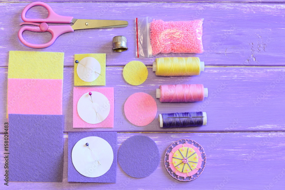 Fototapeta premium Easy craft tutorial to make felt flower. Flower of felt circles and beads, colored felt circles and sheets, scissors, paper templates, thread, needle, beads on a table. Sewing DIY for kids. Top view