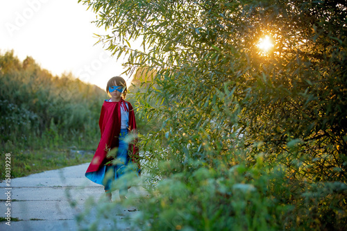 Cute sweet little preschool child  boy  playing superhero on a rural path in a small village