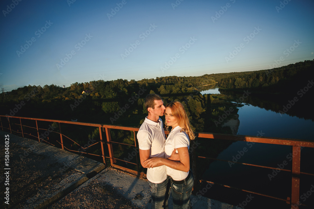 Romantic couple walking on the bridge during the sunset. Summer evening calmness Romantic couple walking on the bridge during the sunset. Summer evening calmness