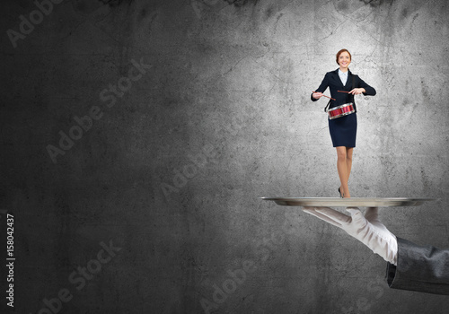 Attractive businesswoman on metal tray playing drums and concrete wall background