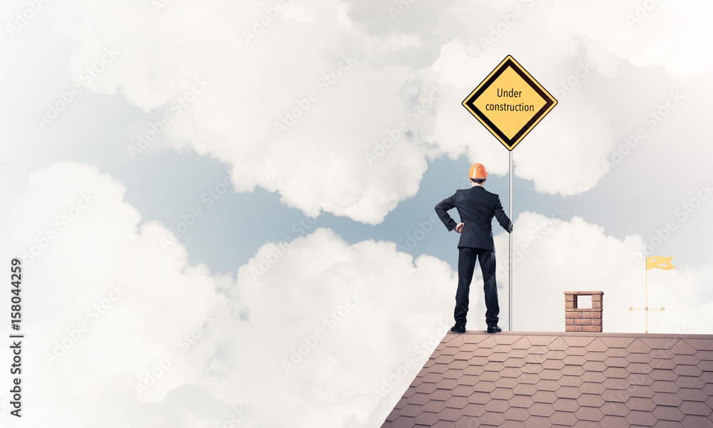 Young businessman on house brick roof holding yellow signboard. Young businessman on house brick roof holding yellow signboard.