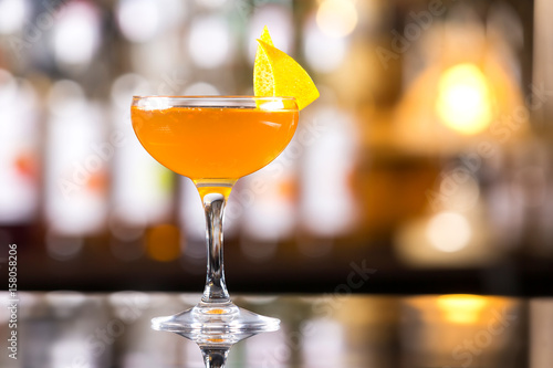 Cuadro en lienzo Glass of orange cocktail decorated with lemon at bar counter background