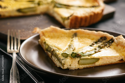 Homemade tart with asparagus and cheese on black background.